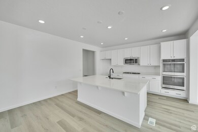 Kitchen with appliances with stainless steel finishes, a sink, white cabinets, a center island with sink, and light wood-type flooring