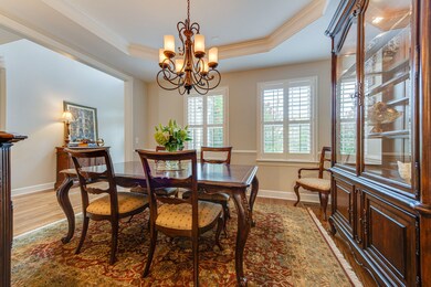 Formal dining view from kitchen includes plantation shutters and elegant chandelier. 