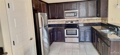 Kitchen with dark stone counters, appliances with stainless steel finishes, dark brown cabinetry, a sink, and backsplash