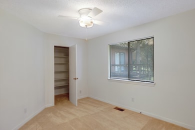Unfurnished bedroom featuring light colored carpet, a textured ceiling, ceiling fan, and a walk in closet
