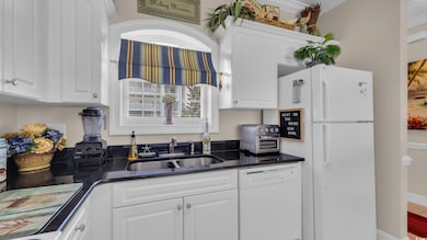 Kitchen featuring white appliances, dark countertops, and white cabinetry