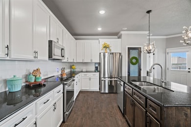 Kitchen with stainless steel appliances, a center island with sink, decorative backsplash, white cabinetry, and dark stone countertops