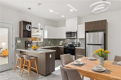 Kitchen featuring appliances with stainless steel finishes, white cabinetry, modern cabinets, a kitchen bar, and decorative backsplash