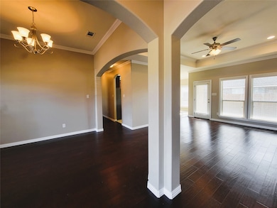 Empty room featuring crown molding, arched walkways, dark wood finished floors, a chandelier, and ceiling fan