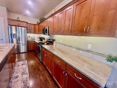 Kitchen with appliances with stainless steel finishes, dark wood-style floors, tasteful backsplash, light stone counters, and brown cabinetry