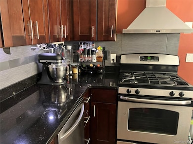 Kitchen with stainless steel appliances, exhaust hood, backsplash, and dark stone countertops
