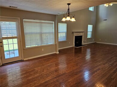 Unfurnished living room featuring wood finished floors, a chandelier, a textured ceiling, and a fireplace with raised hearth