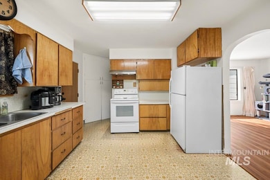 Kitchen with white appliances, light countertops, brown cabinets, arched walkways, and light floors