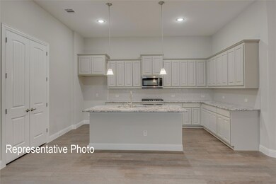 Kitchen with light stone counters, light hardwood / wood-style flooring, a kitchen island with sink, and decorative light fixtures