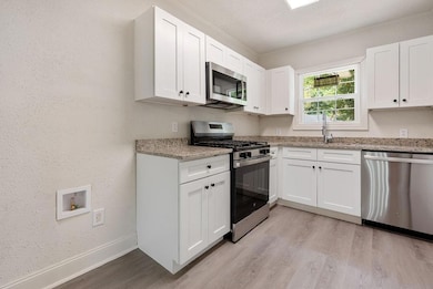Kitchen featuring stainless steel appliances, light wood-style flooring, white cabinetry, and light stone counters