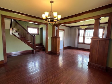 Unfurnished living room featuring dark wood-type flooring, a notable chandelier, crown molding, and ornate columns