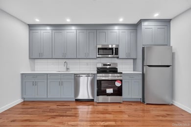 Kitchen featuring appliances with stainless steel finishes, tasteful backsplash, light wood finished floors, gray cabinetry, and recessed lighting