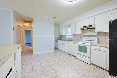 Kitchen featuring white appliances, light countertops, white cabinetry, a textured ceiling, and under cabinet range hood