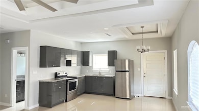 Kitchen featuring stainless steel appliances, gray cabinetry, light countertops, a chandelier, and a tray ceiling