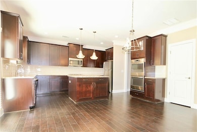 Kitchen with dark hardwood / wood-style floors, stainless steel appliances, backsplash, and hanging light fixtures