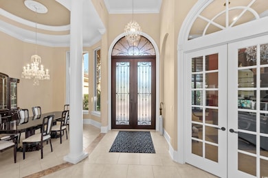 Foyer entrance with french doors, a chandelier, light tile patterned floors, and crown molding