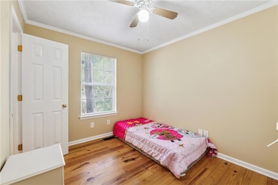 Bedroom featuring light wood finished floors, ornamental molding, and ceiling fan