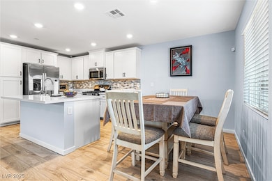 Kitchen with appliances with stainless steel finishes, light wood-type flooring, decorative backsplash, light countertops, and white cabinets