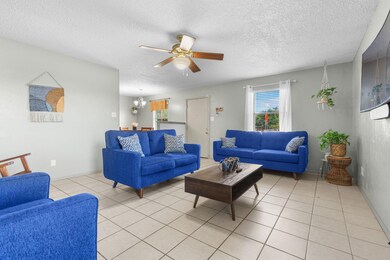 Tiled living room featuring a textured ceiling and ceiling fan with notable chandelier