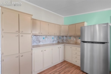 Kitchen featuring freestanding refrigerator, cream cabinetry, light countertops, crown molding, and light wood finished floors