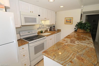 Kitchen with white appliances, white cabinetry, recessed lighting, dark stone counters, and light tile patterned floors