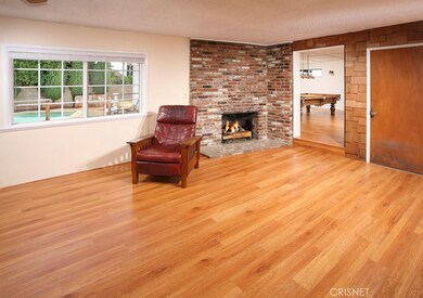 The open and spacious family room offers a ceiling fan, dramatic floor-to-ceiling raised hearth brick fireplace and gleaming modern wood flooring.