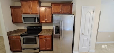Kitchen with stainless steel appliances, brown cabinetry, and light tile patterned flooring