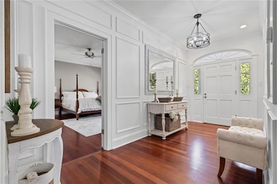 Entryway with dark wood-style floors, a decorative wall, ornamental molding, and a chandelier