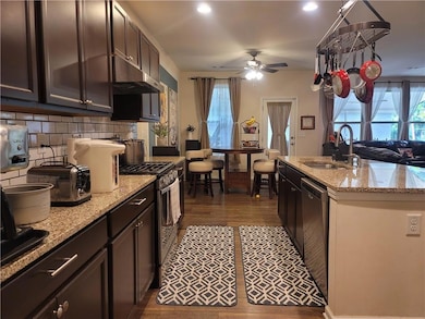 Kitchen featuring appliances with stainless steel finishes, dark wood-type flooring, light stone counters, under cabinet range hood, and open floor plan