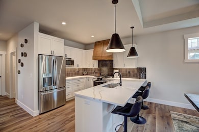 Kitchen featuring appliances with stainless steel finishes, a kitchen bar, a peninsula, white cabinetry, and hanging light fixtures