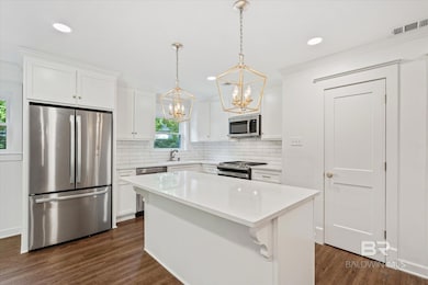 Kitchen with appliances with stainless steel finishes, pendant lighting, backsplash, white cabinetry, and dark wood-type flooring