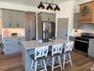 Kitchen with appliances with stainless steel finishes, tasteful backsplash, gray cabinetry, and light stone counters