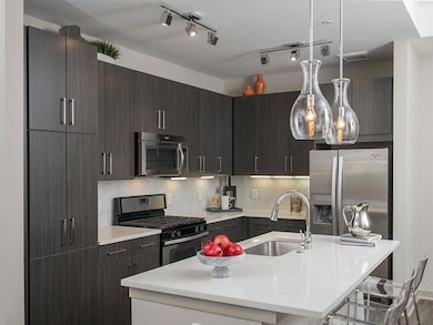 Kitchen featuring a center island with sink, stainless steel appliances, rail lighting, sink, and pendant lighting
