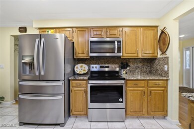 Kitchen featuring appliances with stainless steel finishes, dark stone countertops, light tile patterned floors, decorative backsplash, and ornamental molding