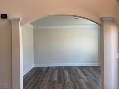 Empty room with arched walkways, crown molding, dark wood-style flooring, and decorative columns