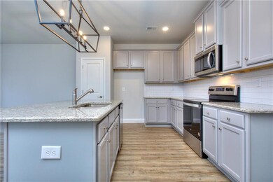 Kitchen with appliances with stainless steel finishes, gray cabinets, light wood-type flooring, tasteful backsplash, and a chandelier