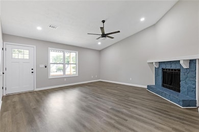 Unfurnished living room with ceiling fan, wood finished floors, a stone fireplace, vaulted ceiling, and recessed lighting