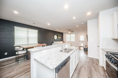 Modern kitchen with white cabinetry, granite countertops, stainless steel appliances, and a contrasting dark accent wall. Open plan layout with ample lighting and wood-look flooring.