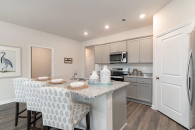 Kitchen with appliances with stainless steel finishes, gray cabinets, dark wood-type flooring, a sink, and a breakfast bar