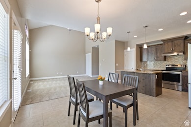 Dining room with light tile patterned flooring, a chandelier, lofted ceiling, a textured ceiling, and recessed lighting