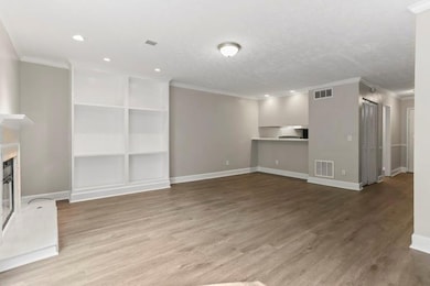 Unfurnished living room featuring ornamental molding, light wood-style floors, a glass covered fireplace, and a textured ceiling