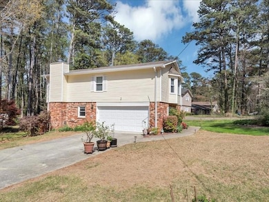 View of property exterior with driveway, a chimney, an attached garage, brick siding, and a lawn