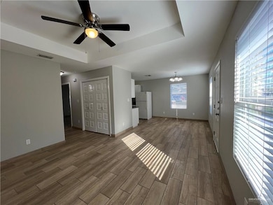 Unfurnished living room with a raised ceiling, a chandelier, wood finished floors, and ceiling fan