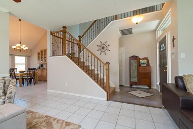Enter the home through a steel paneled door surrounded by transom windows into this welcoming foyer with ceramic tile flooring, fresh, neutral paint, updated lighting, and a split staircase with wrought iron balusters and wood railings.