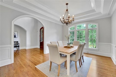 Dining area with arched walkways, a chandelier, a tray ceiling, ornamental molding, and light wood-style floors