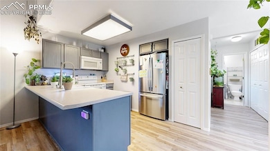 Kitchen featuring white appliances, a peninsula, light wood-type flooring, light countertops, and gray cabinetry