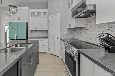 Kitchen with appliances with stainless steel finishes, white cabinets, tasteful backsplash, decorative light fixtures, and light hardwood / wood-style flooring