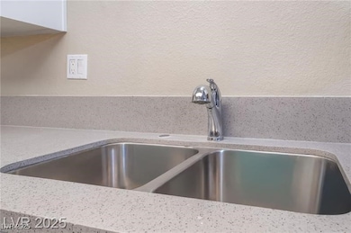Kitchen view of light stone counters, a textured wall, and white cabinetry