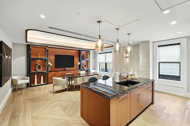 Kitchen featuring dark stone counters, decorative light fixtures, brown cabinetry, an island with sink, and recessed lighting