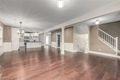 Open concept living room / dining room featuring a chandelier, dark hardwood flooring, and ornate columns, with a view of the kitchen.
